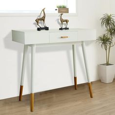 a white table with two small statues on top and a potted plant next to it