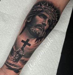 a man's arm with a cross and jesus on the cross tattoo in black and grey