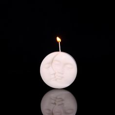 a candle with a face on it sitting in front of a black background and reflecting light