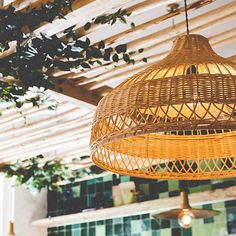 a wicker light fixture hanging from a ceiling in a room with green tiles on the walls