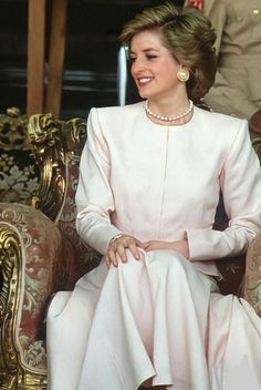 a woman sitting on top of a chair wearing a white dress and pearl necklaces