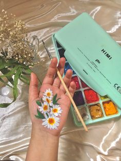 a person's hand with paint and flowers painted on their fingers next to an artist's palette