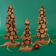 three wooden christmas trees are next to a red ornament on a green background