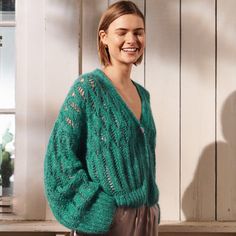 a woman standing in front of a white wall wearing a green sweater