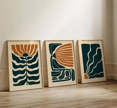 three framed art prints in different colors on a wooden floor next to a white wall