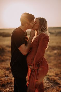 a man and woman kissing each other in the middle of an open field at sunset