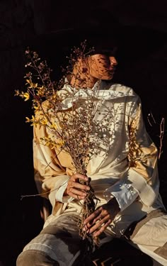 a woman in a white dress and hat holding a plant with yellow flowers on it