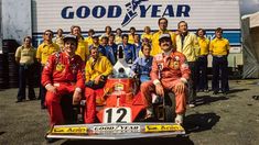 a group of men sitting on top of a race car in front of a sign