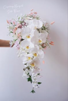 a bridal bouquet with white orchids, pink and yellow flowers on it is held by a woman's hand