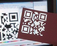 a person holding up a piece of paper with a qr code on it in front of a computer screen