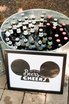 a metal bucket filled with bottles of beer on top of a brick floor next to a sign