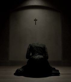 a woman sitting on the floor in front of a cross