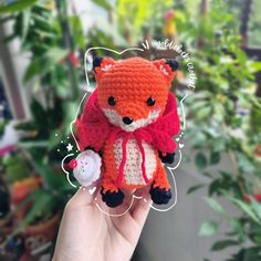 a small crocheted fox doll is held up in front of some plants