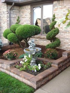 a small fountain in the middle of a flower bed next to a brick building with windows