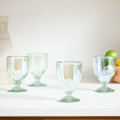 three empty wine glasses sitting on a counter next to a vase and an apple in a bowl