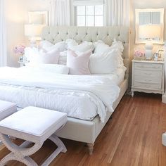 a bedroom with white bedding and pillows on the headboard, footstools, nightstands and lamps