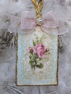 a glass ornament with pink roses on it and a bow hanging from the front