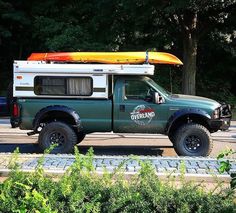 a green truck with a kayak on the roof is parked in front of some bushes