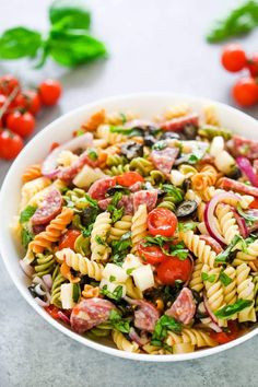 a bowl filled with pasta salad on top of a table next to tomatoes and basil