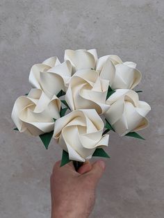 a hand holding a bunch of white flowers on top of a cement floor next to a wall