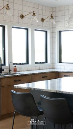 a kitchen with three windows and four bar stools in front of the counter top