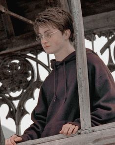 a young man wearing glasses and a hoodie looks out from an ornate iron balcony