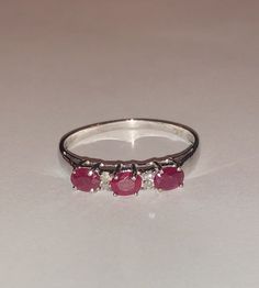 Beautifully vintage. Solid, stamped 10K White Gold Band Ring. 10K tends to be more durable than 14K. Natural oval cut, red Ruby gemstones and round cut Diamonds. Ring size approximately 7 Perfect as an anniversary, July birthstone, stack ring. Classic Three Stone Round Ruby Ring, Classic Three Stone Ruby Promise Ring, Classic Red Three Stone Rings, Classic Red Three-stone Ring, Classic Three Stone Ruby Ring In 14k Gold, Classic 14k Gold Three-stone Ruby Ring, Classic 14k Gold Three Stone Ruby Ring, Classic White Gold Ruby Ring Birthstone, Classic White Gold Ruby Birthstone Ring