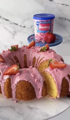 a bundt cake with pink icing and strawberries on top next to a can of ice cream