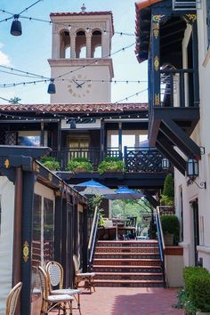 an outdoor patio with tables and chairs under a clock tower on the top of a building