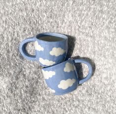 two coffee mugs with clouds painted on them sitting on the floor next to each other