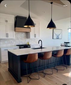 a kitchen with an island and three pendant lights hanging over the counter top, along with four bar stools