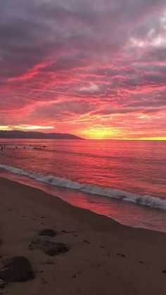 the sun is setting over the ocean and people are swimming in the water at the beach