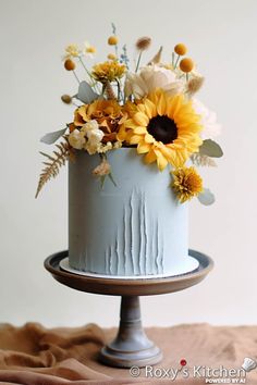 a blue cake with sunflowers and other flowers on it sitting on a table