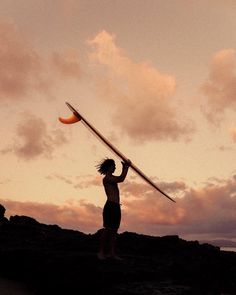 a woman holding a surfboard over her head while standing on top of a hill