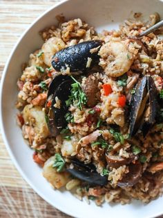 a white bowl filled with rice and mussels on top of a wooden table