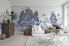 a living room filled with furniture next to a wall covered in ship paintings on the walls