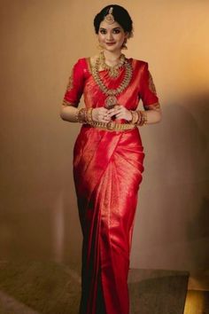 a woman in a red sari with gold jewelry on her neck and hands behind her back