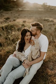 a man and woman are sitting on the ground together, smiling at each other as they hold their hands up