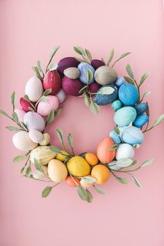 an easter wreath made out of colored eggs and leaves on a pink background with the words happy easter written below it