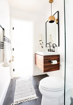 a white toilet sitting next to a bathroom sink under a mirror on top of a wooden cabinet