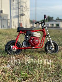 a small red motorcycle parked on top of a grass covered field next to a building