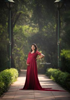 a pregnant woman in a long red dress poses for a photo with her hands on her hips