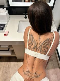 a woman with tattoos on her back sitting in front of a sink