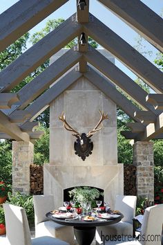 an outdoor dining area with white chairs and a black table surrounded by deer head mounted on the wall