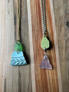 two necklaces with different designs on them sitting on top of a wooden table next to each other