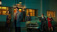 a group of men and women standing in front of an old fashioned car at night