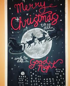 a chalkboard sign with santa's sleigh flying over the city at night