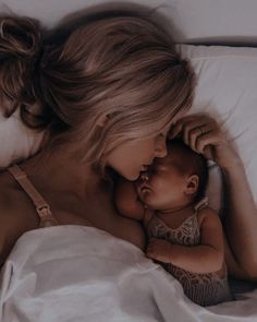 a woman laying in bed holding a baby next to her head and touching it's cheek