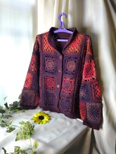 a crocheted jacket is hanging on a clothes hanger next to a sunflower