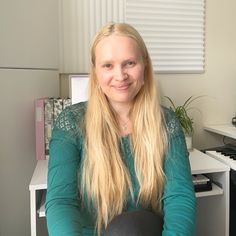 a woman with long blonde hair sitting in front of a computer desk, smiling at the camera